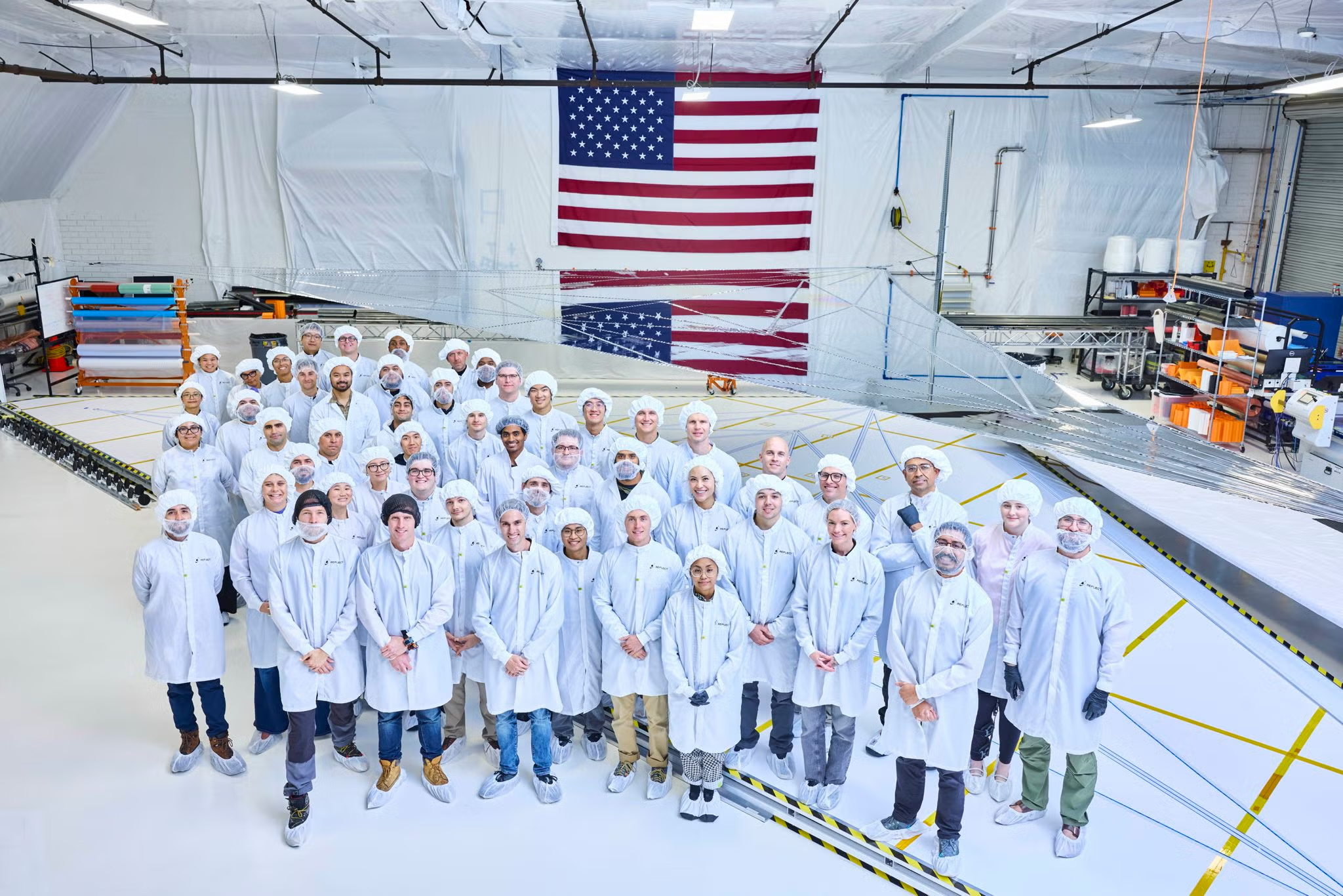 The Reflect Orbital team in cleanroom suits in front of an American flag